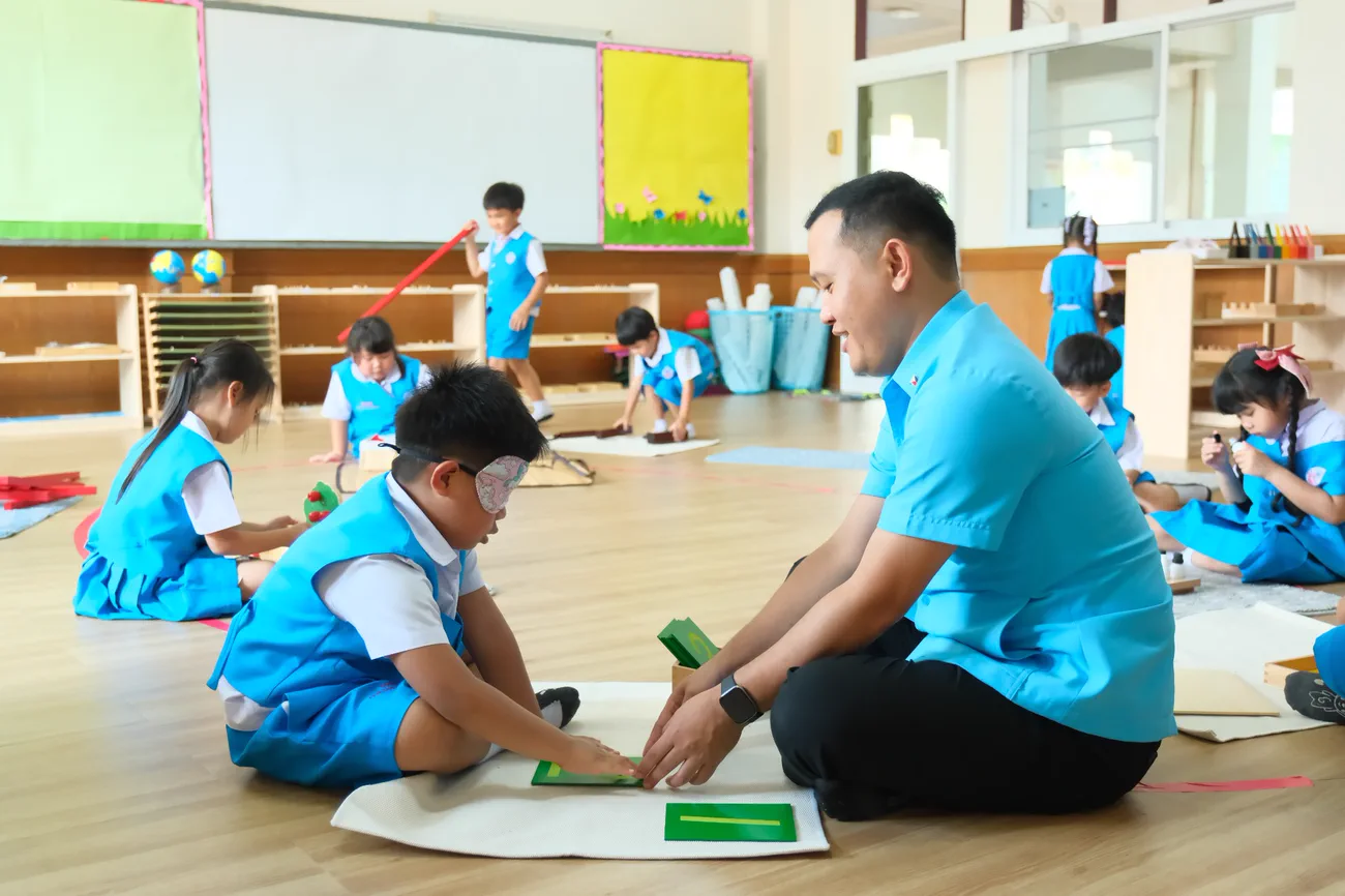 เด็กและคุณครูทำกิจกรรมบนพื้นในห้องมอนเตสซอรี่